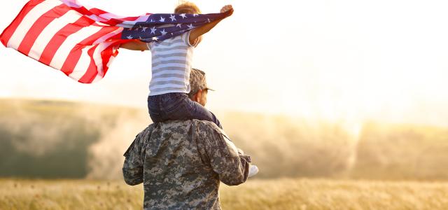 Excited child sitting with american flag on shoulders of father reunited with family